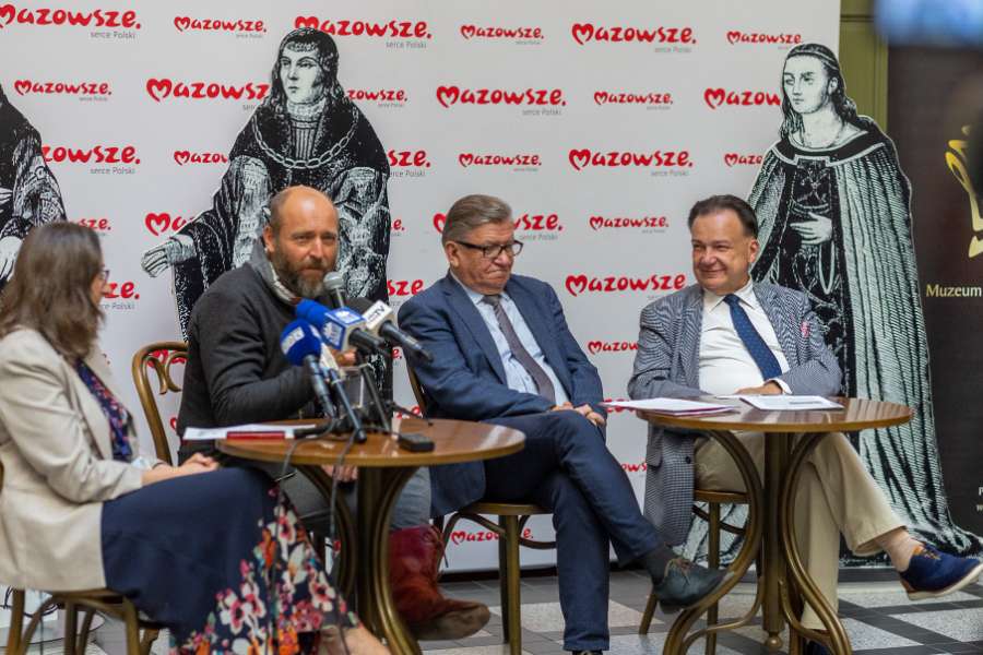 Uczestnicy panelu dyskusyjnego przy stolikach na tle logotypów Mazowsze oraz grafik historycznych