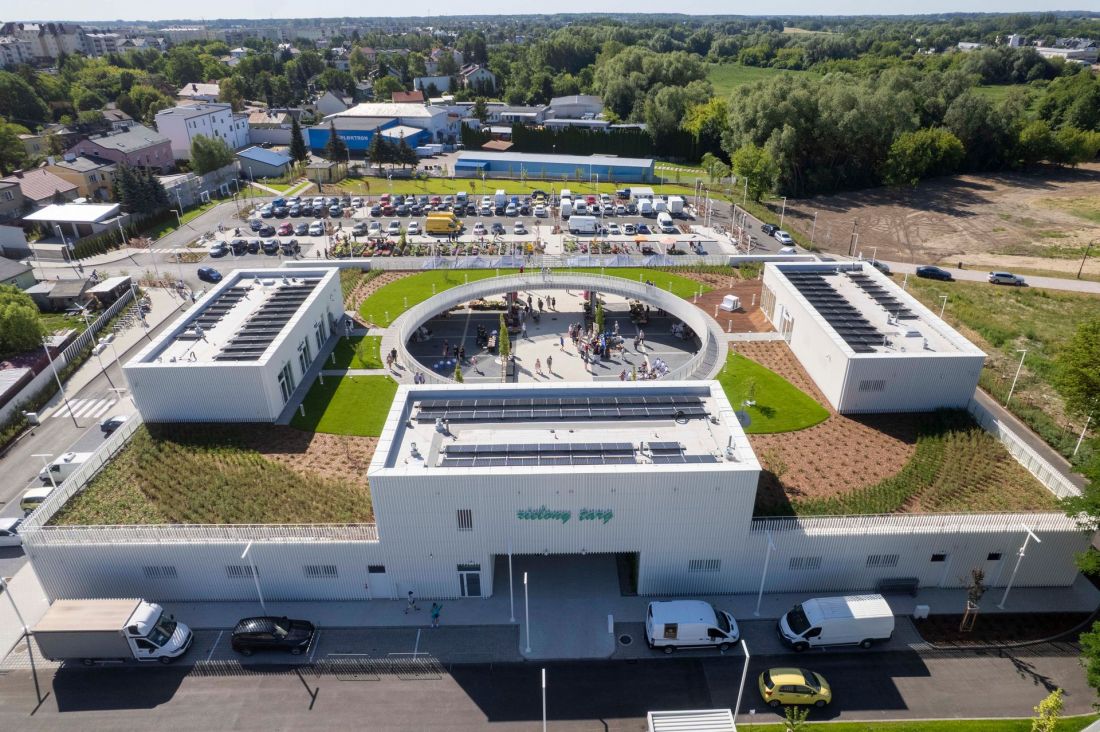 Widok z góry na Zielony Targ w Ciechanowie. Budynek w kształcie litery U z dużym, okrągłym wycięciem w zadaszeniu nad wewnętrznym placem oraz widocznym zielonym dachem użytkowym.